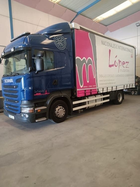 Camión Scania azul oscuro con remolque blanco, anunciando