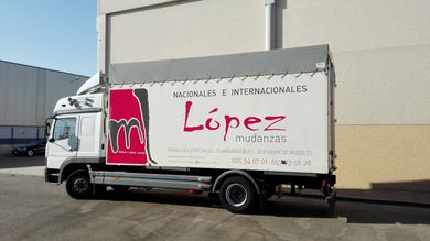 Camión de mudanzas López, de color blanco, con logo y texto en color rojo, estacionado al aire libre.