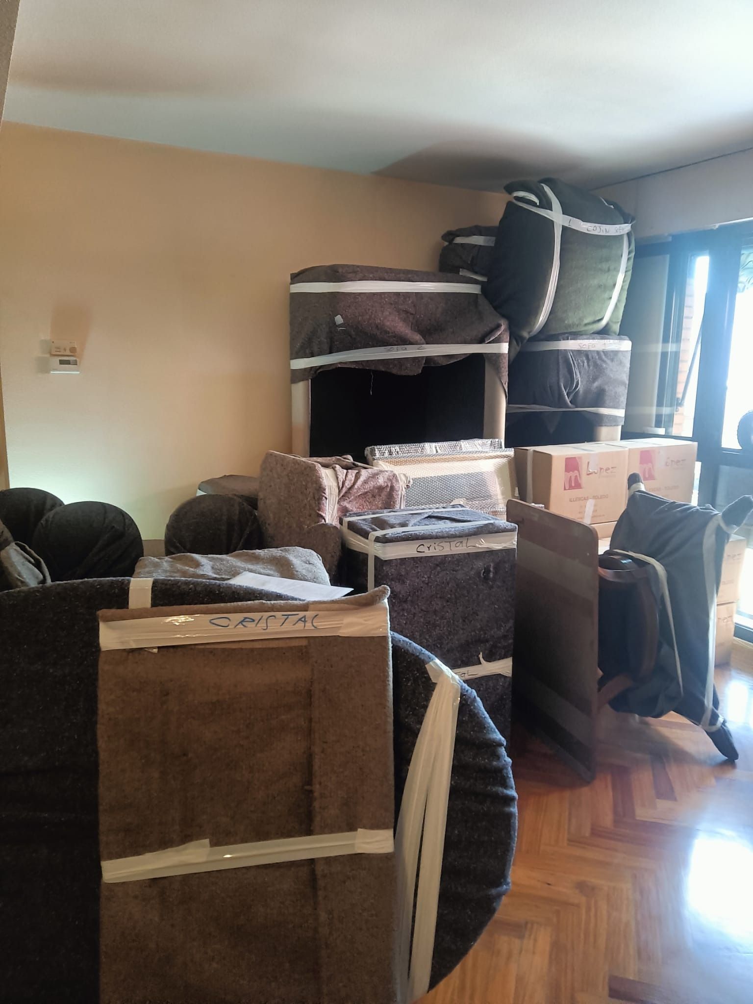 Día de mudanza. Muebles y cajas envueltos llenan una habitación con paredes claras y suelos de madera.