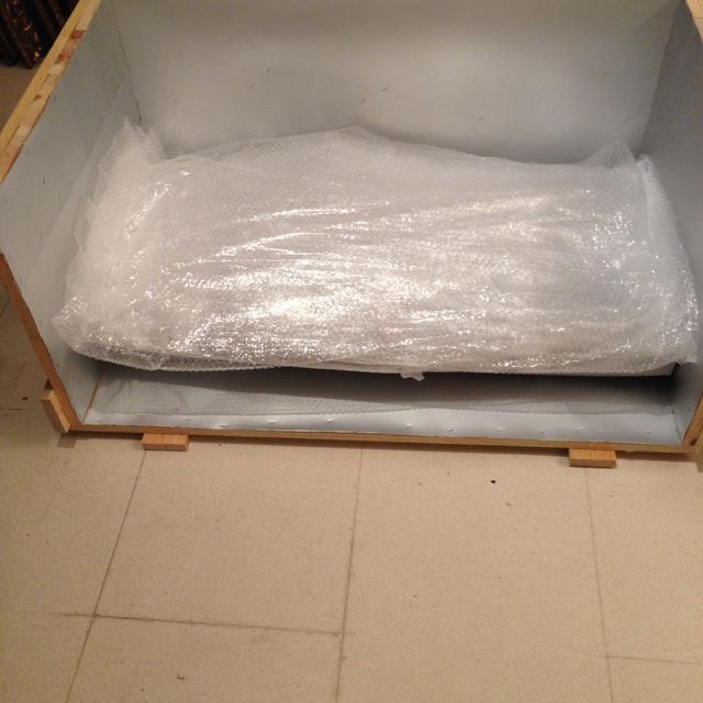 Caja de madera que contiene un paquete envuelto en plástico de burbujas.