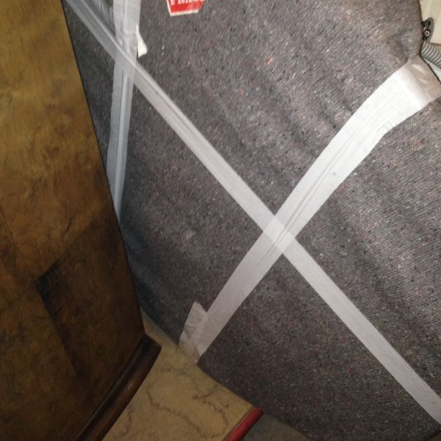 Objeto cubierto de tela gris envuelto con cinta blanca; cerca de un gabinete de madera y el piso.