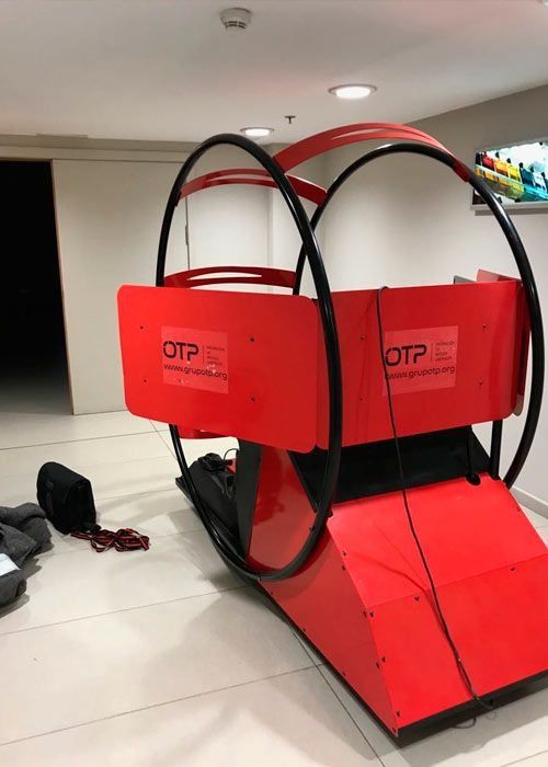 Máquina de ejercicios roja y negra en un espacio con paredes blancas. La máquina tiene dos aros.