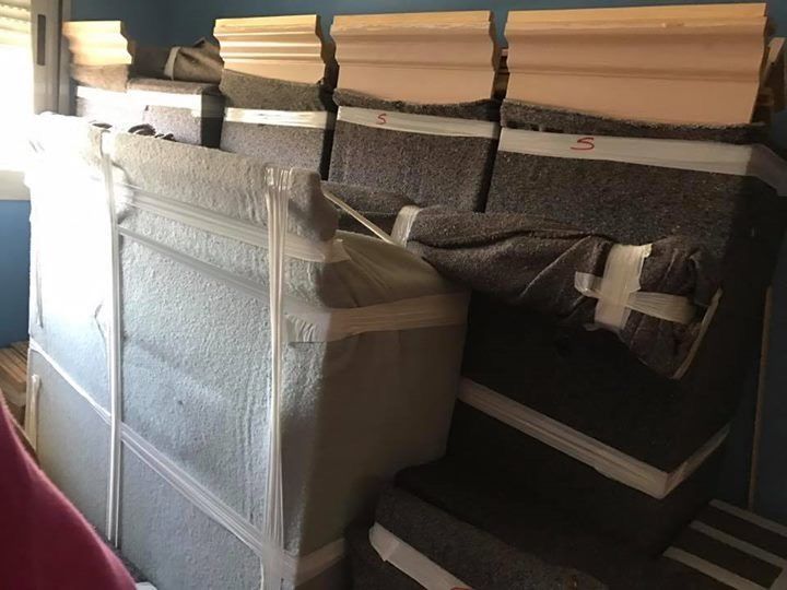 Una pila de objetos envueltos, posiblemente muebles, contra una pared azul. Se ven algunas molduras.