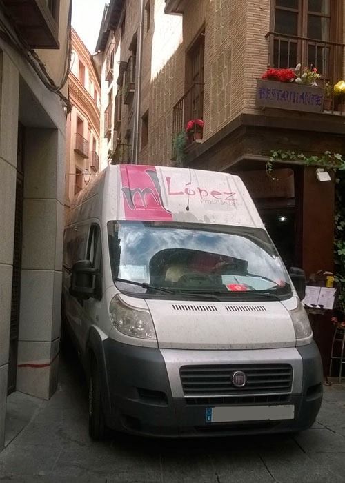 Furgoneta de reparto blanca estacionada en una calle estrecha, entre edificios en Toledo, España.