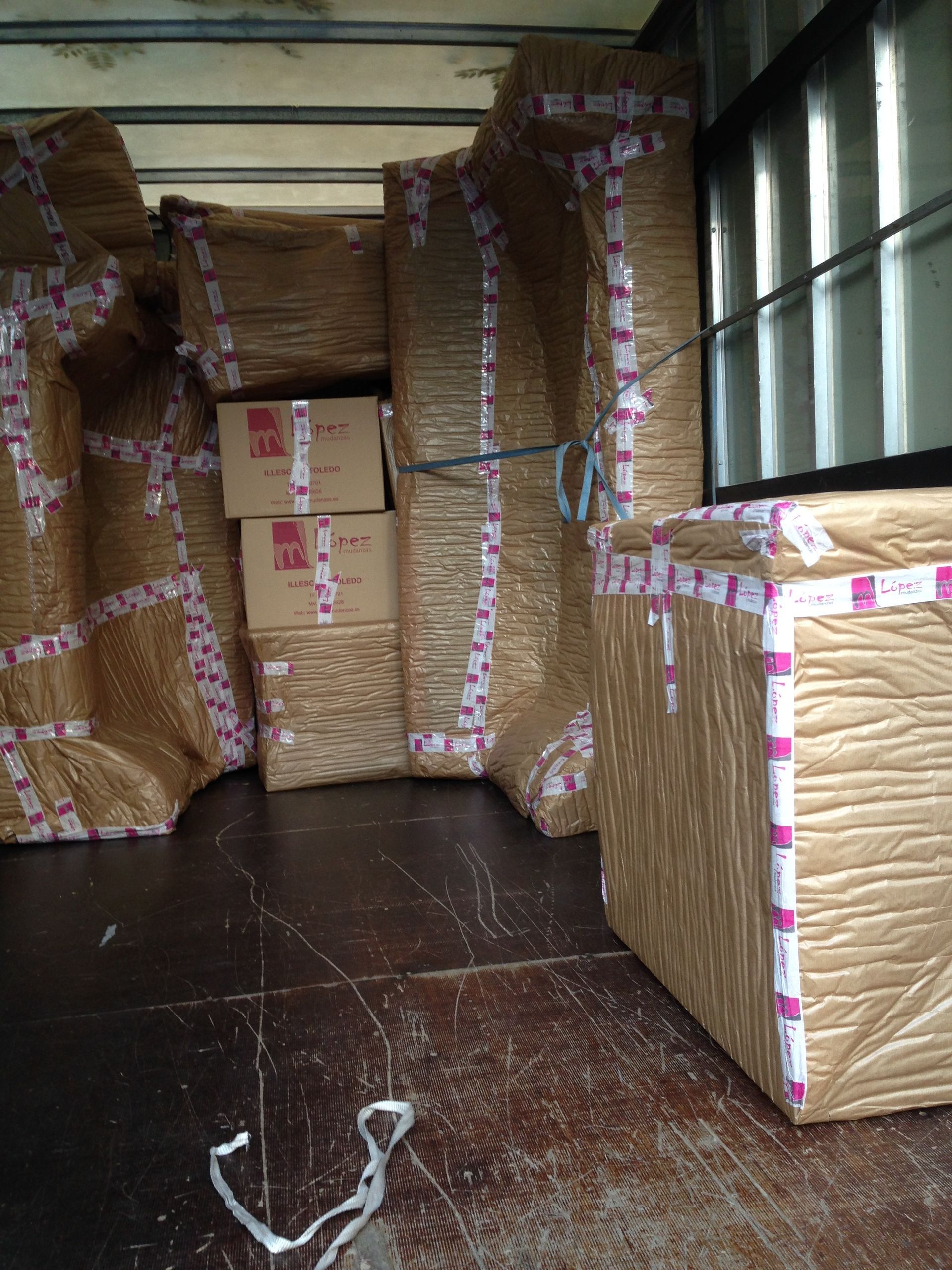 Muebles y cajas embalados en un camión de mudanzas, envueltos en papel marrón y asegurados con cinta adhesiva.