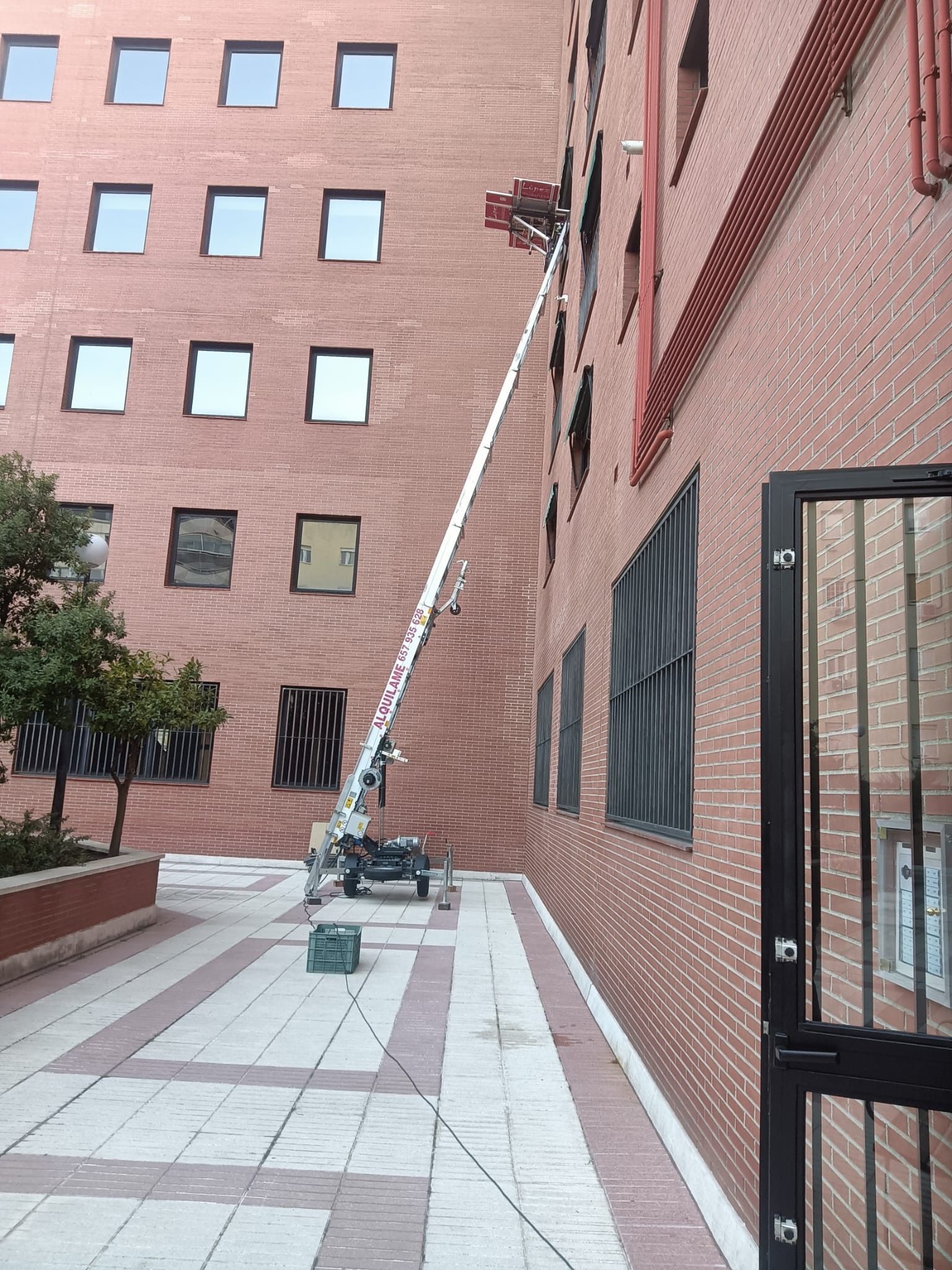 Una plataforma elevadora se extiende hasta un edificio de ladrillos para trabajar en las ventanas.