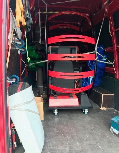Interior de furgoneta de carga roja; una máquina roja asegurada para transporte, herramientas y equipo visibles.