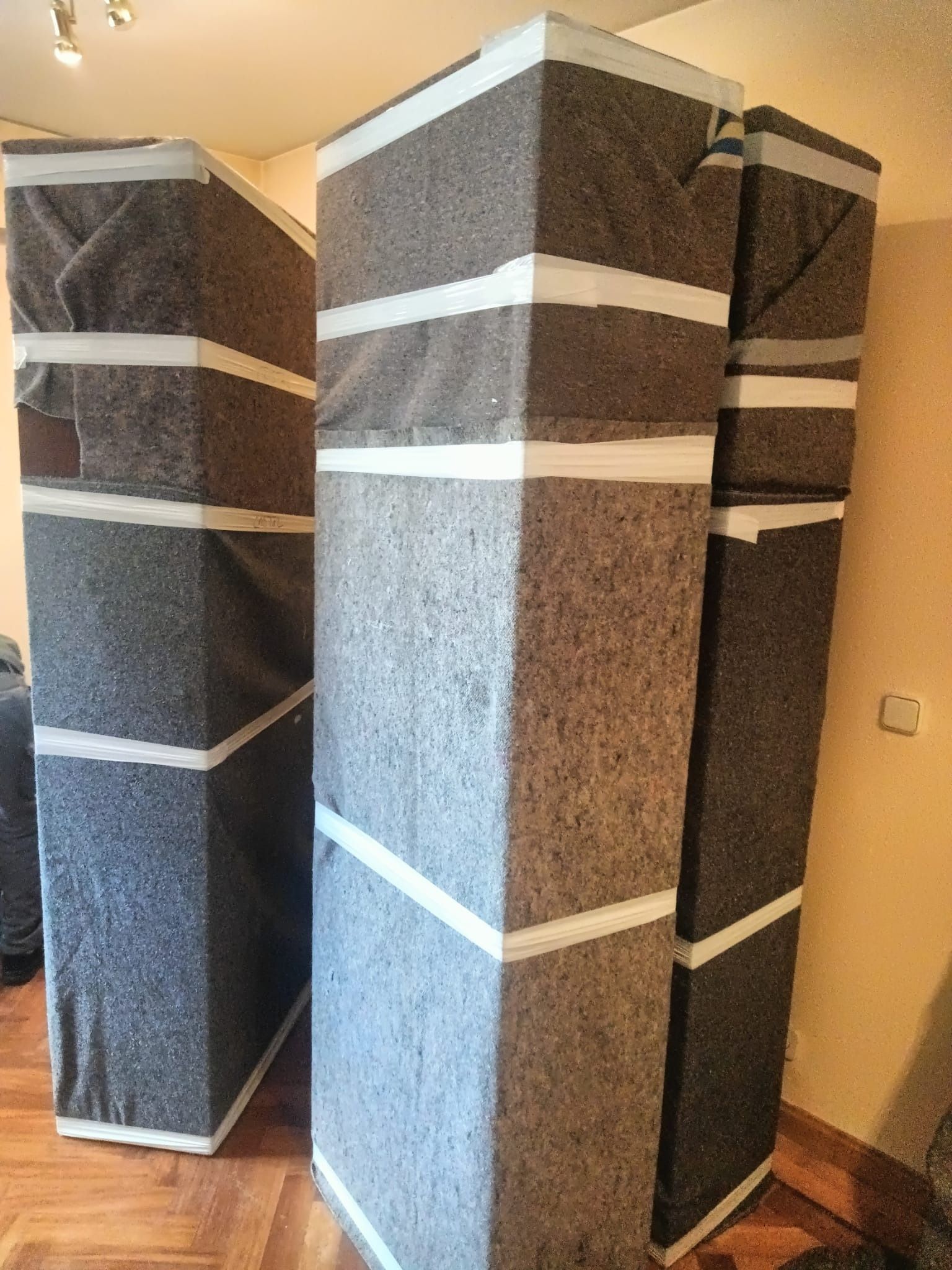 Tres paneles acústicos altos y rectangulares cubiertos de tela oscura y sellados con rayas blancas, en una habitación.