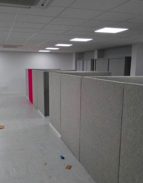 Filas de paredes grises de cubículos en una oficina vacía. Se ve una sección rosa de la pared.