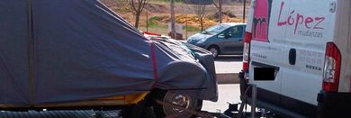 Un vehículo cubierto con una lona gris, junto a una camioneta blanca con escrito 