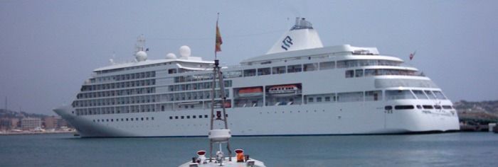 Gran crucero blanco en un puerto, con un pequeño barco en primer plano.