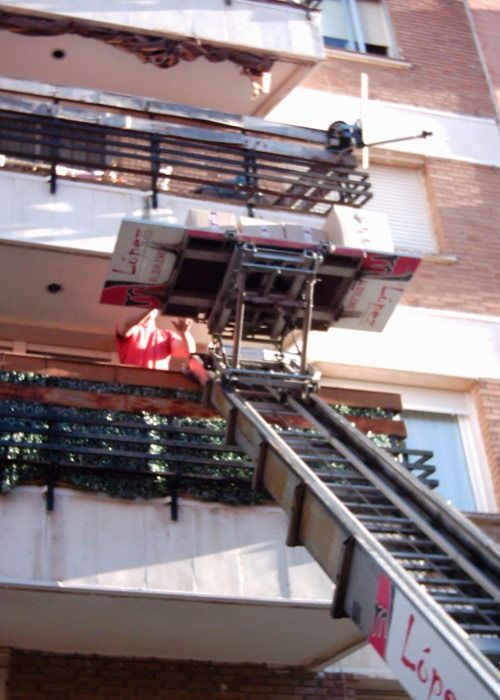 Una plataforma de camión en movimiento en un balcón, con una rampa que se extiende hacia abajo; edificio de ladrillo al fondo.