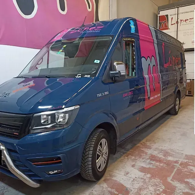 Furgoneta de reparto azul con marcas rosas y grises, estacionada dentro de un edificio.