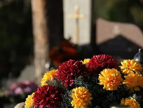 Un ramo de flores rojas y amarillas en un cementerio, con una cruz y lápidas en el fondo.