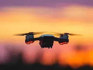 Dron en vuelo contra un cielo de atardecer vibrante con tonos naranjas y morados.
