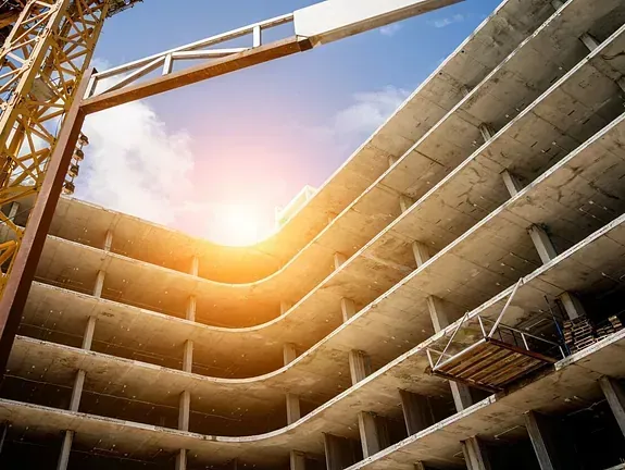 Sitio de construcción de un edificio de varios pisos en construcción, con una grúa amarilla contra un cielo azul brillante con el sol brillando.