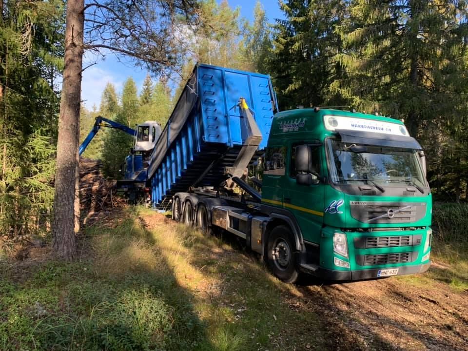 Vihreä kuorma-auto sinisellä kippilavalla metsässä. 