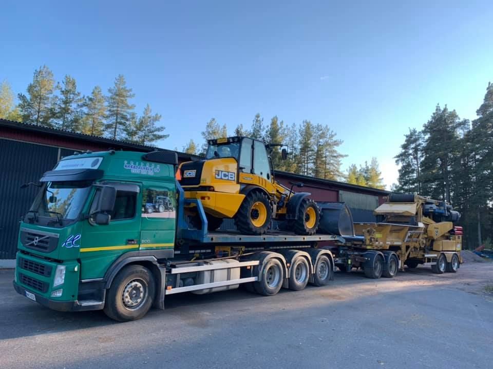 Vihreä kuorma-auto kuljettaa keltaista työkonetta.