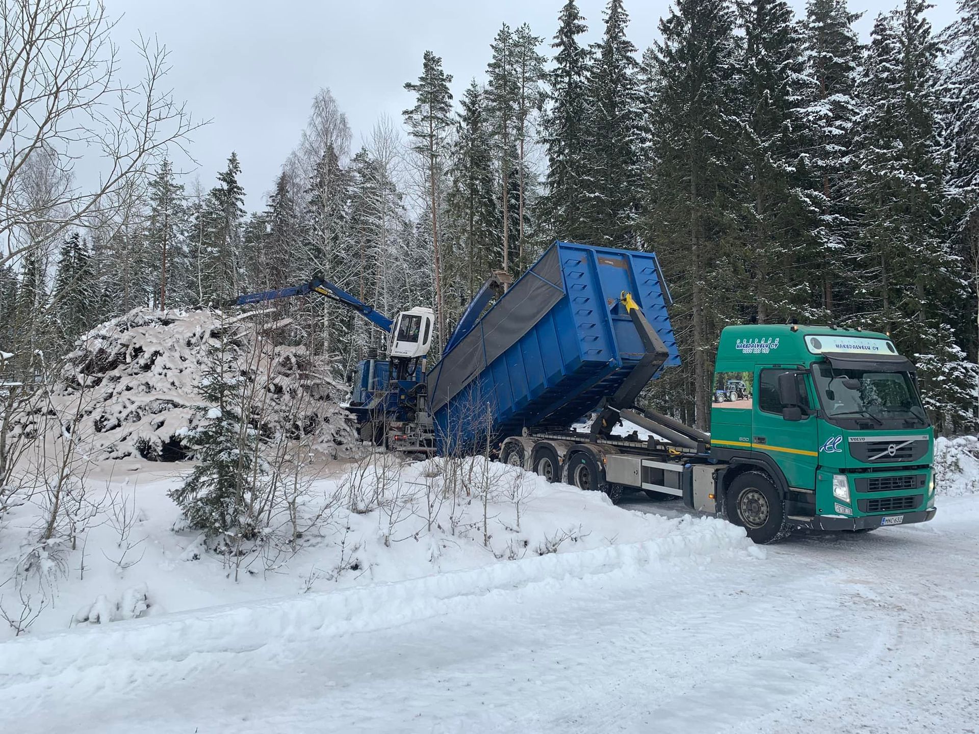 Vihreä kippiauto hakee metsästä lastia talvella.