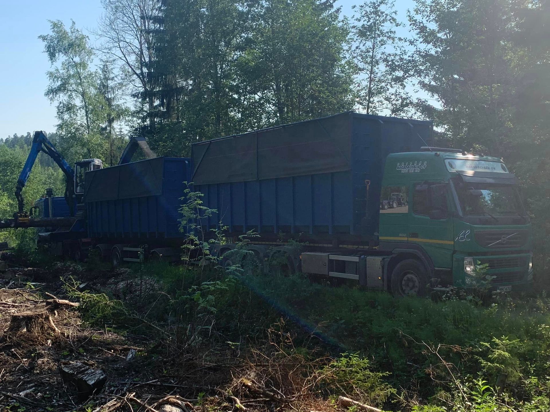 Sinivihreä kuorma-auto metsässä lastattavana.