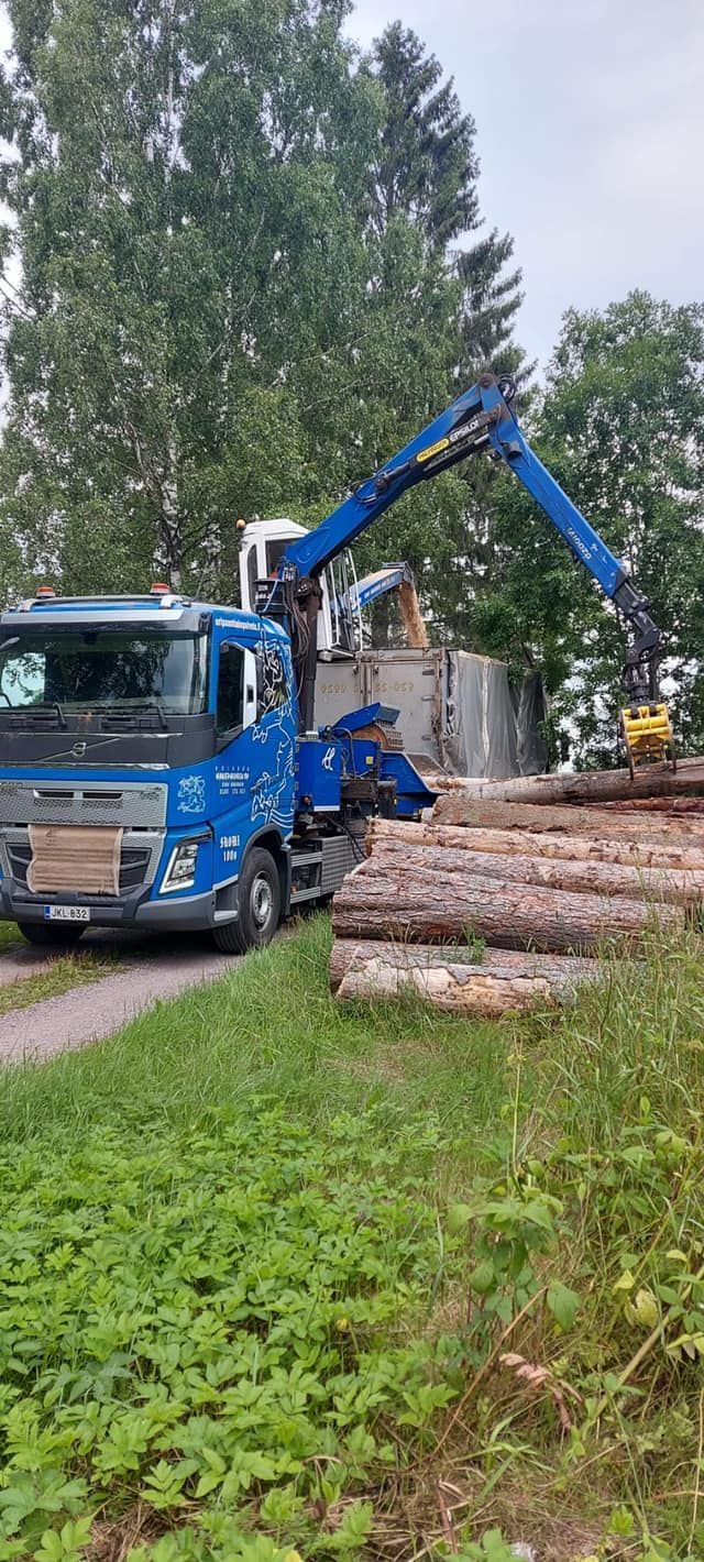 Sininen kuorma-auto, johon on kiinnitetty nosturi, lastataan puilla.