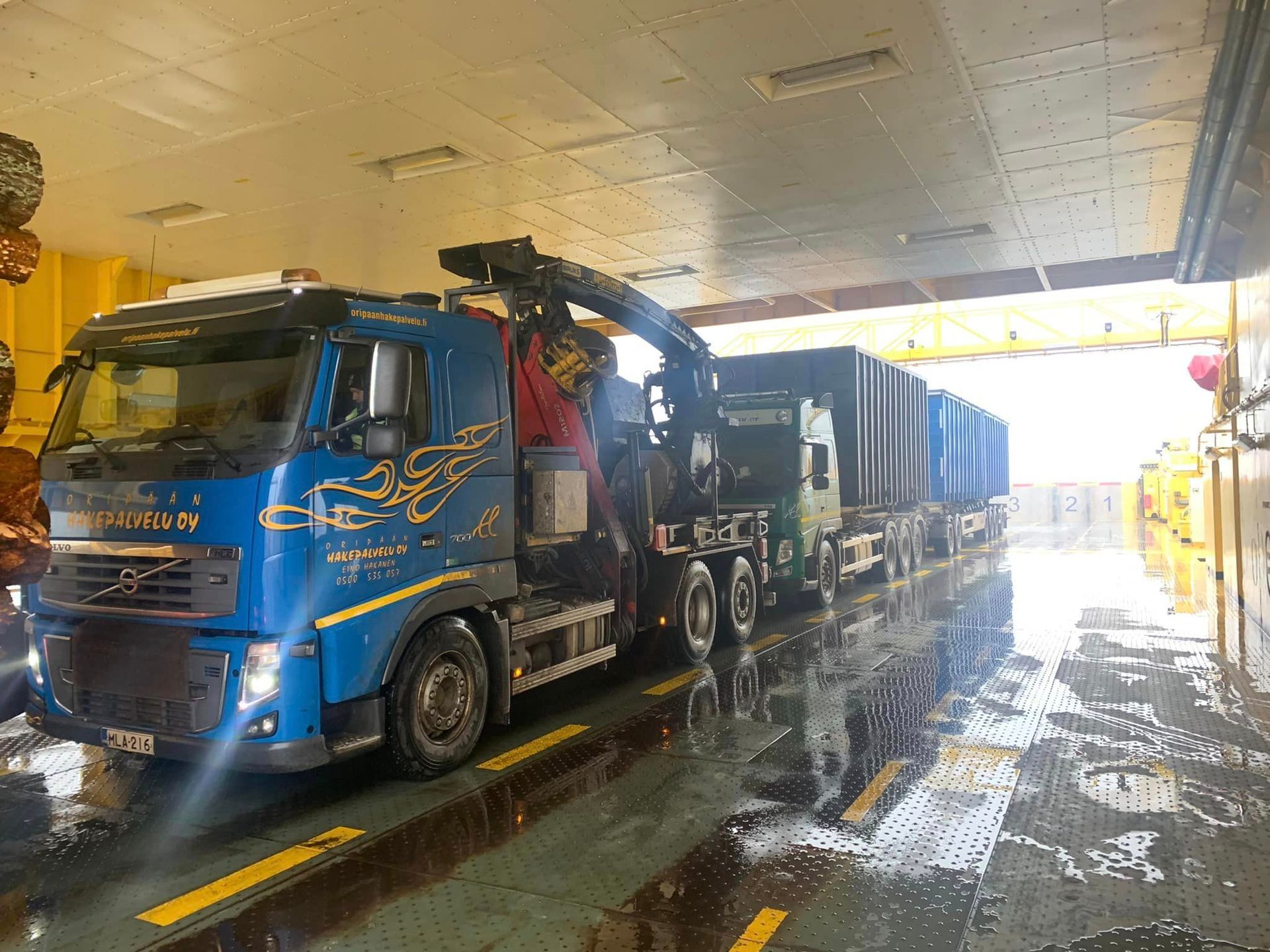 Sininen kuorma-auto, jonka takana on nosturi, on pysäköitynä hallissa.