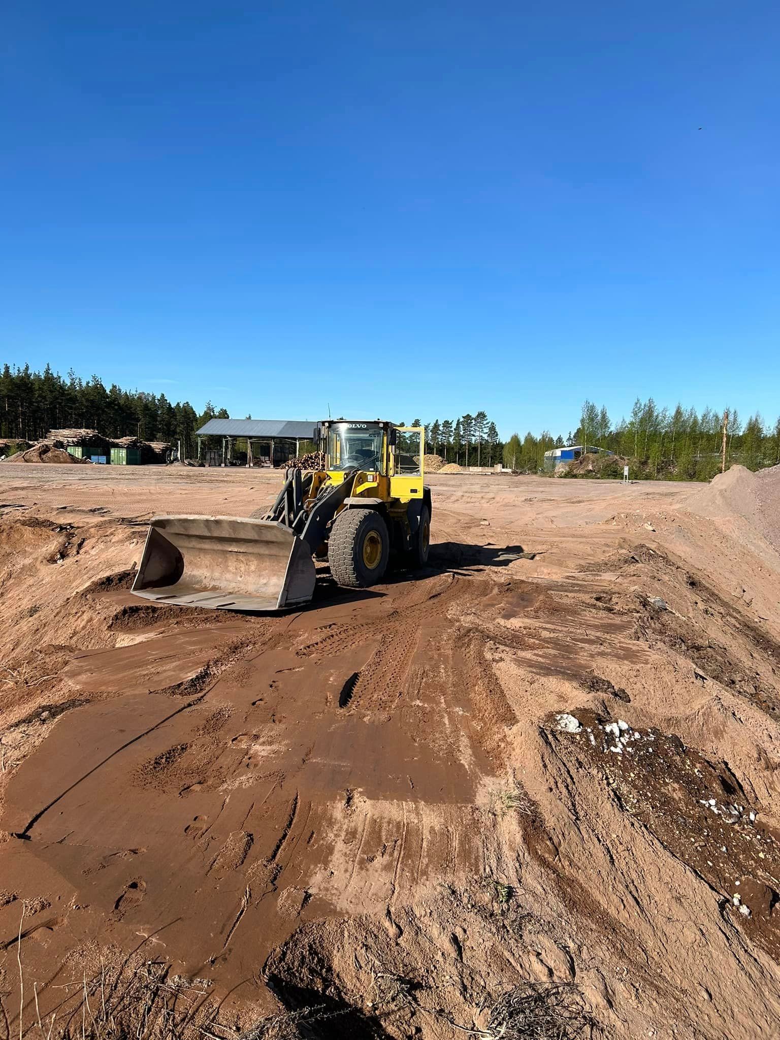 Keltainen puskutraktori ajaa hiekkakentän läpi.