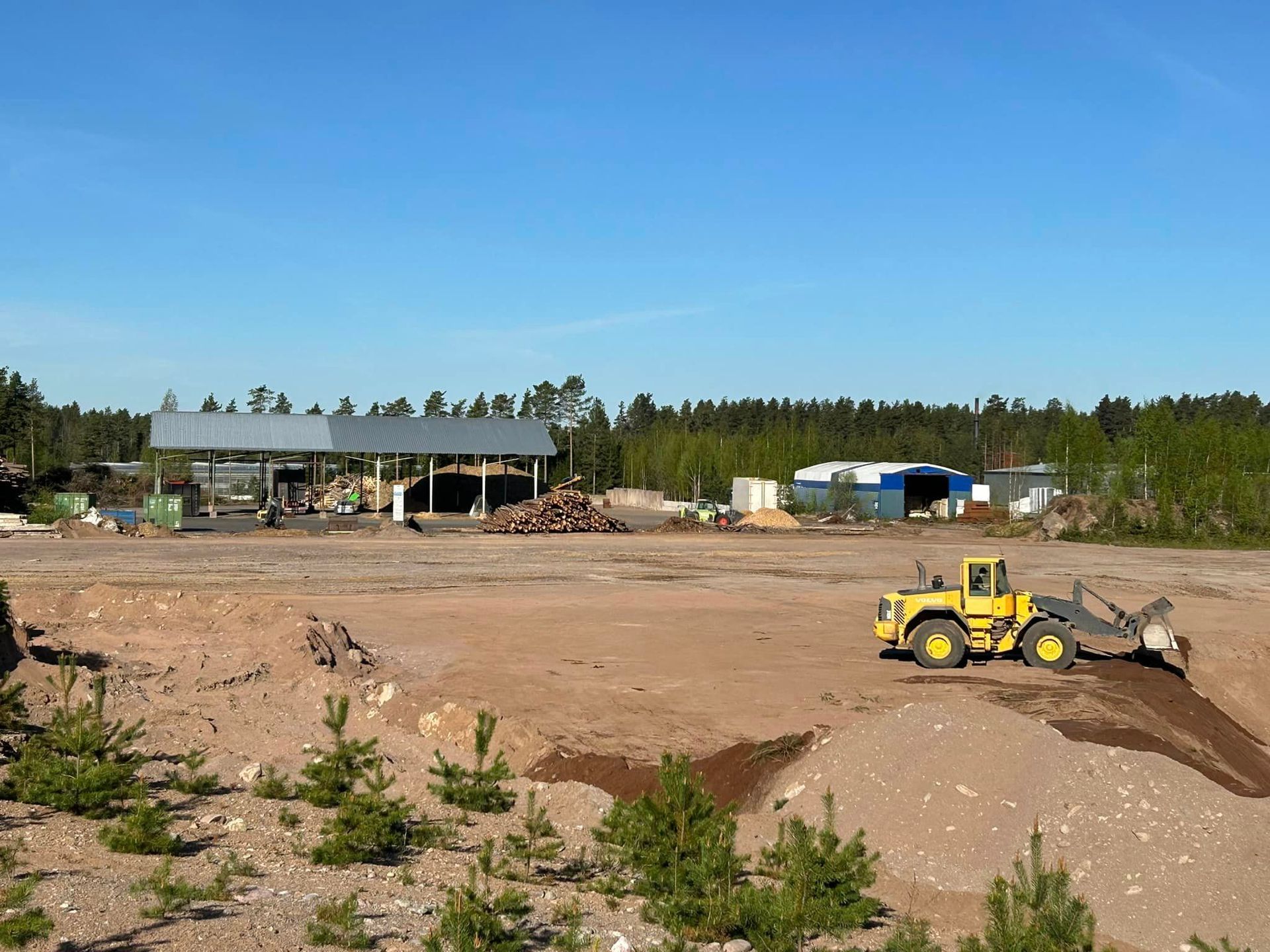 Keltainen puskutraktori ajaa hiekkakentän läpi.