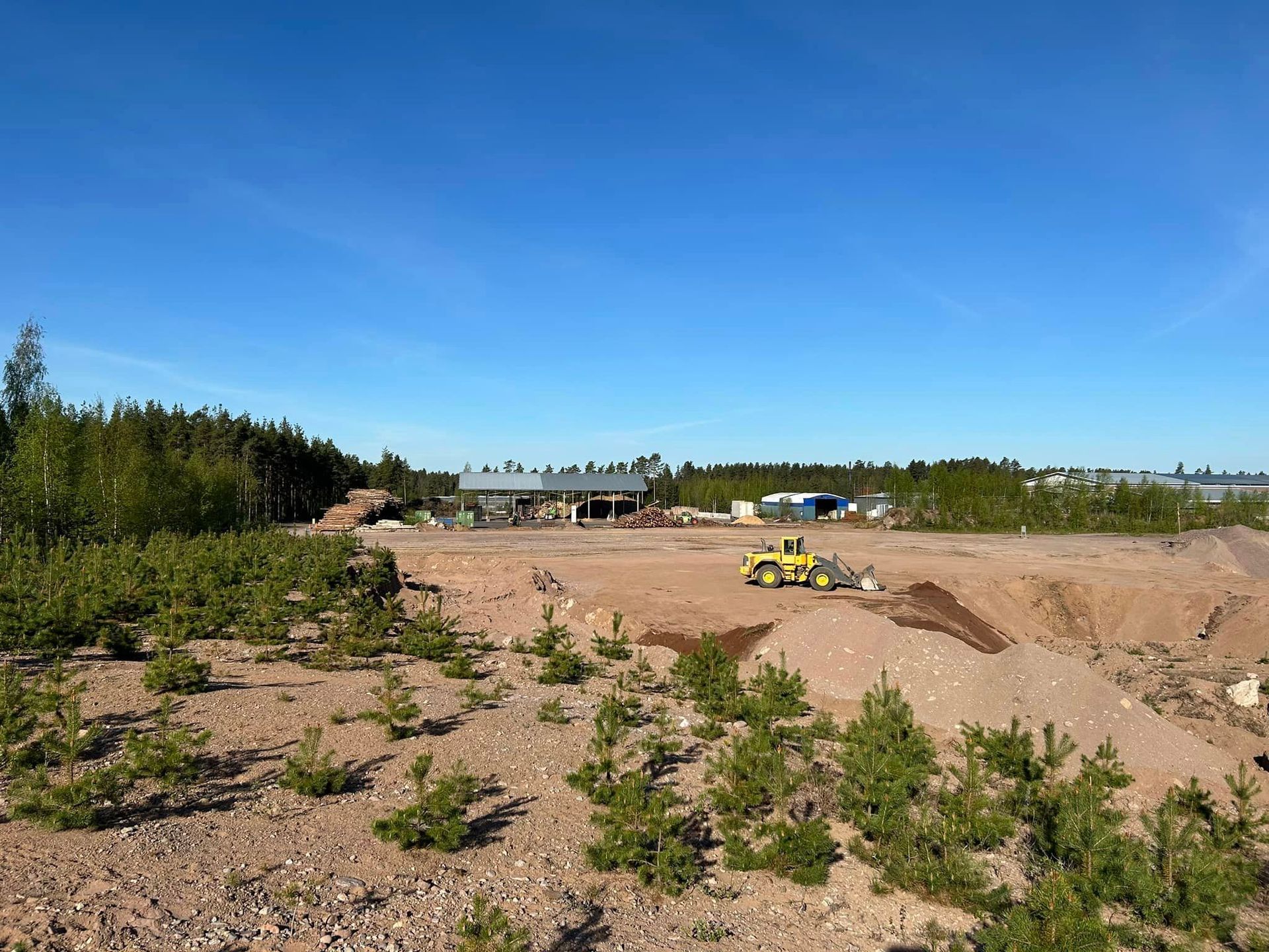 Keltainen puskutraktori ajaa hiekkakentän läpi.