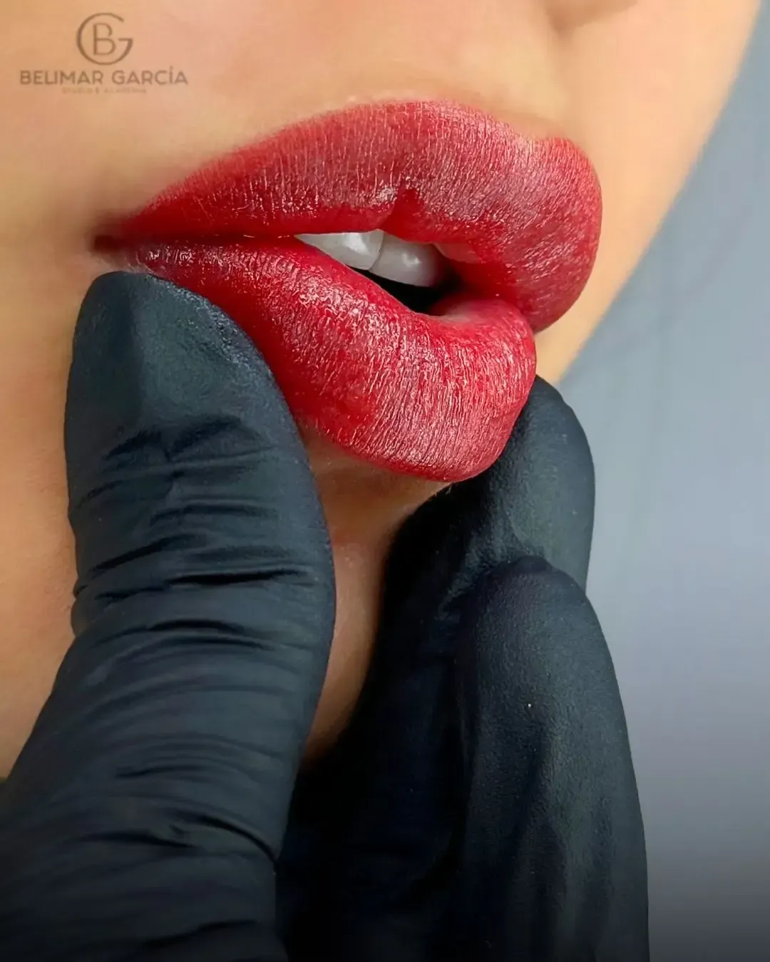 Primer plano de unos labios rojos brillantes sostenidos suavemente por una mano enguantada de negro.