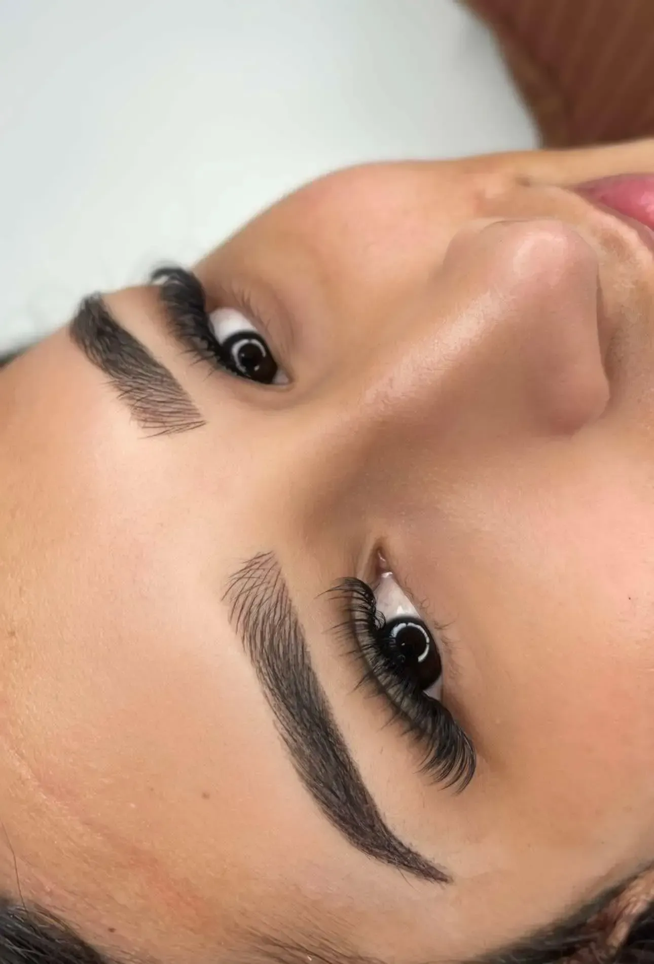 Primer plano de un rostro con cejas definidas y pestañas largas, girado lateralmente sobre un fondo liso.