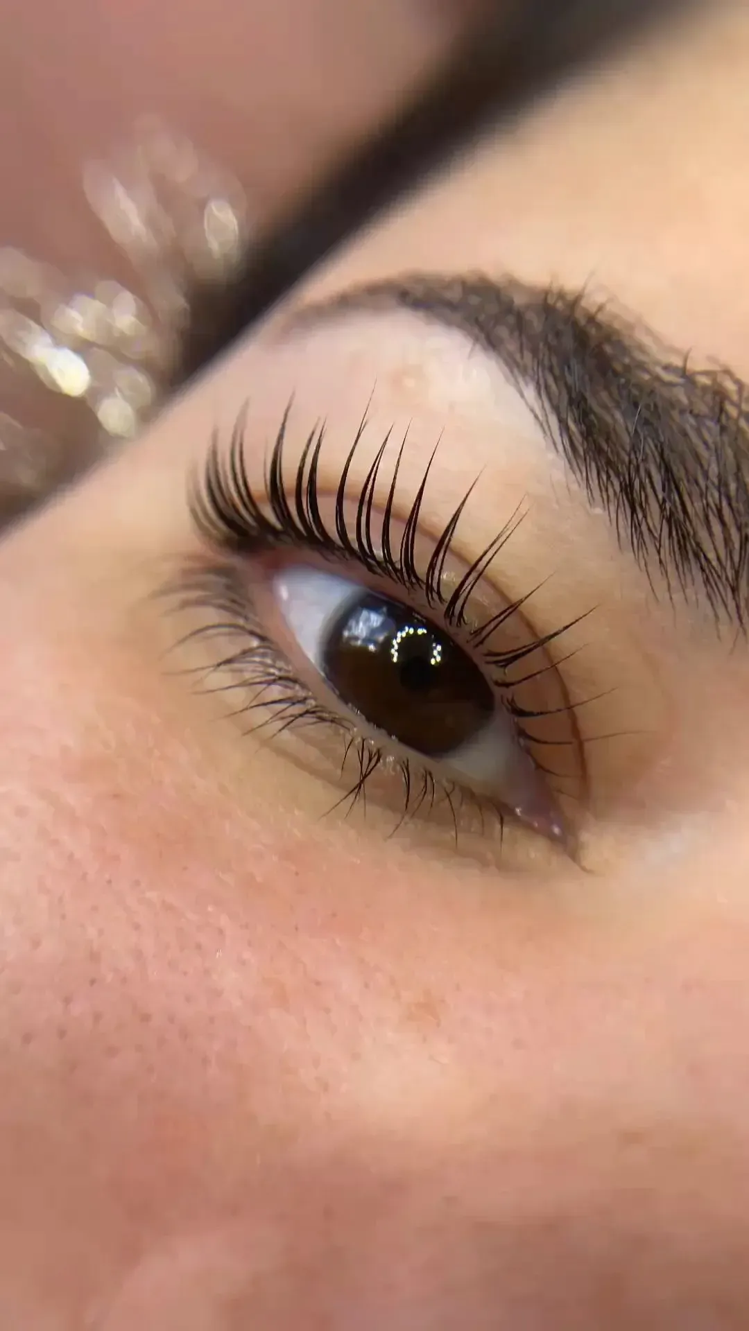 Primer plano de un ojo marrón con pestañas largas y rizadas y cejas bien arregladas.