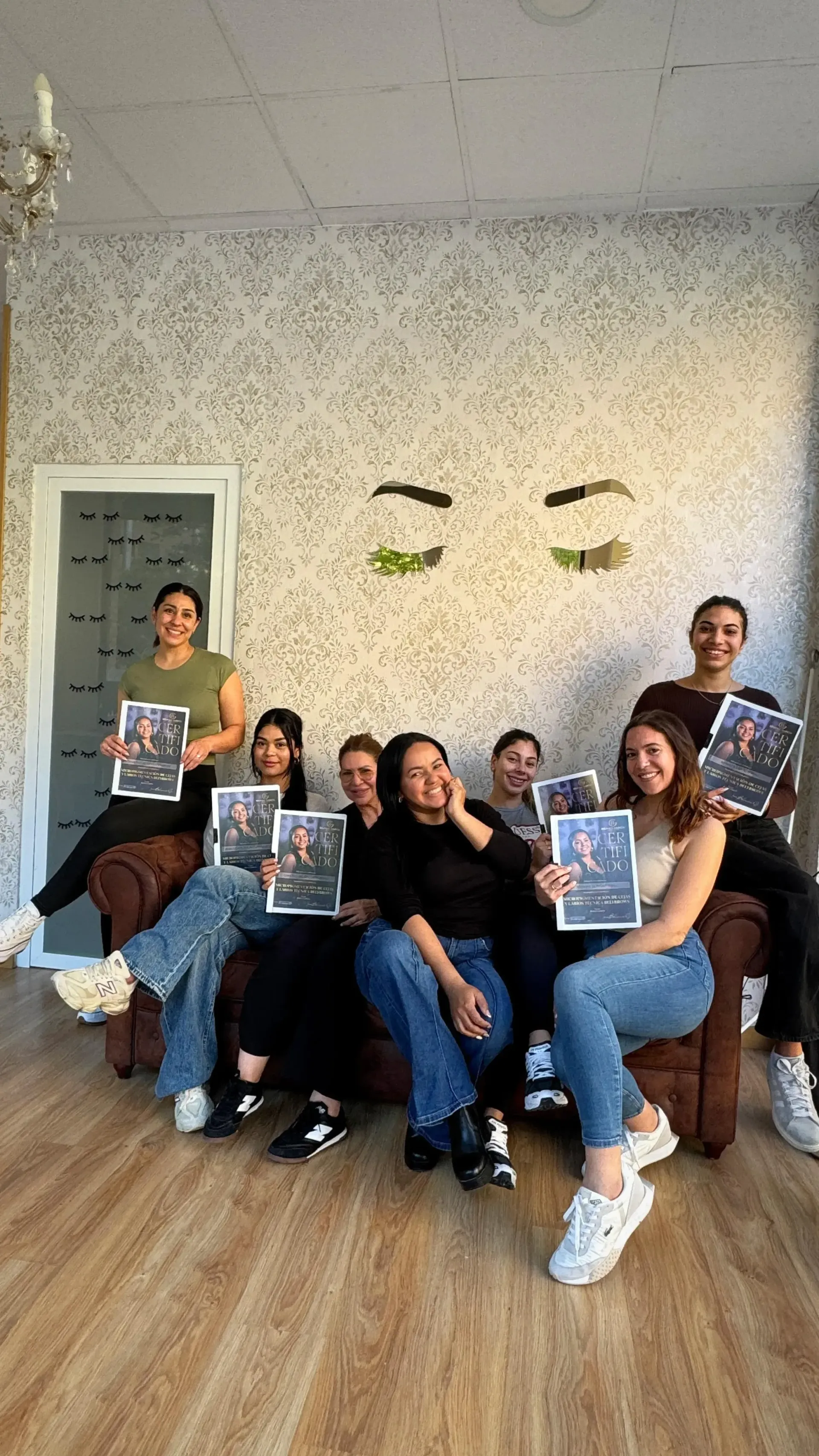 Un grupo de personas posando en una habitación luminosa, sentadas y de pie en sillas con carteles coloridos.