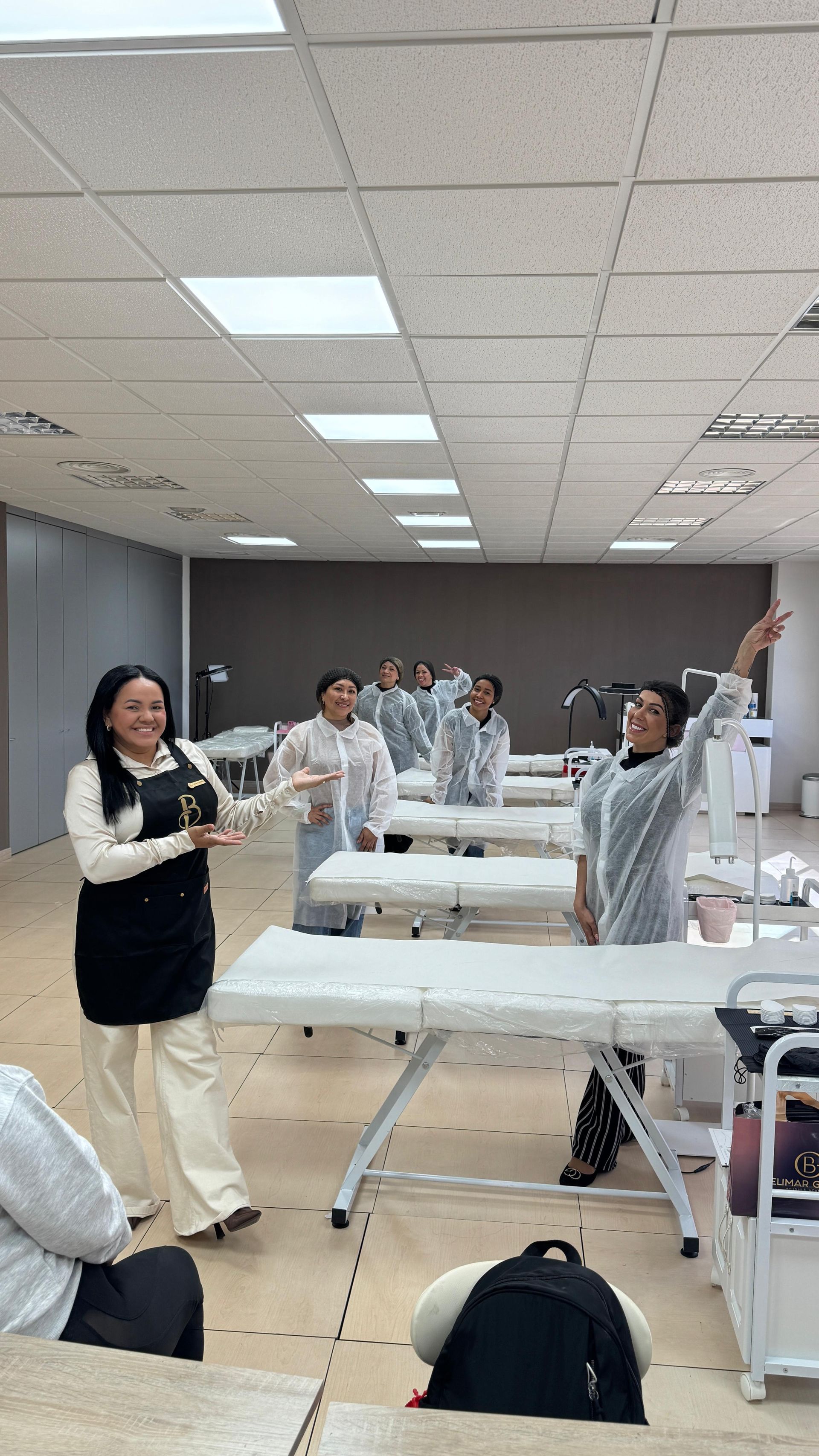 En un aula, varias personas bailan o se estiran juntas junto a largas mesas bajo luces fluorescentes.