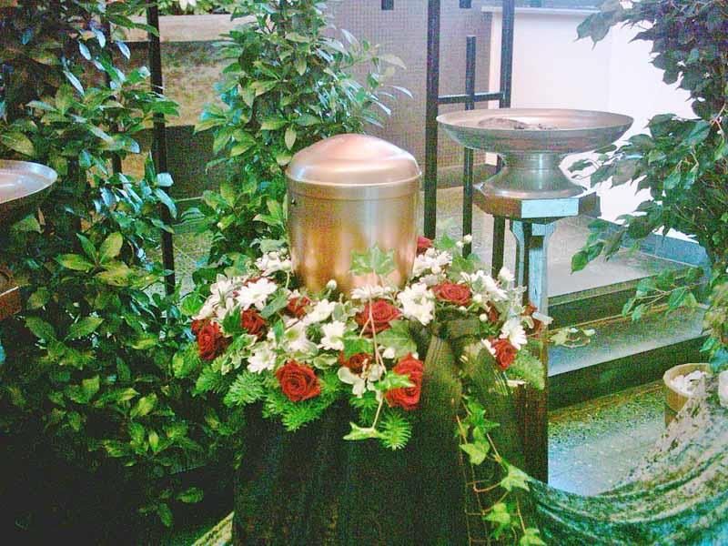 Eine Kupferurne ist von Blumen und Pflanzen umgeben