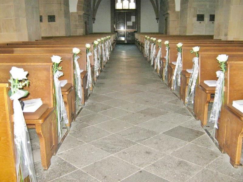 Reihen von Holzbänken in einer mit weißen Blumen geschmückten Kirche