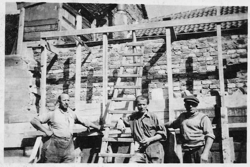 Ein Schwarzweißfoto von drei Männern, die vor einer Backsteinmauer stehen