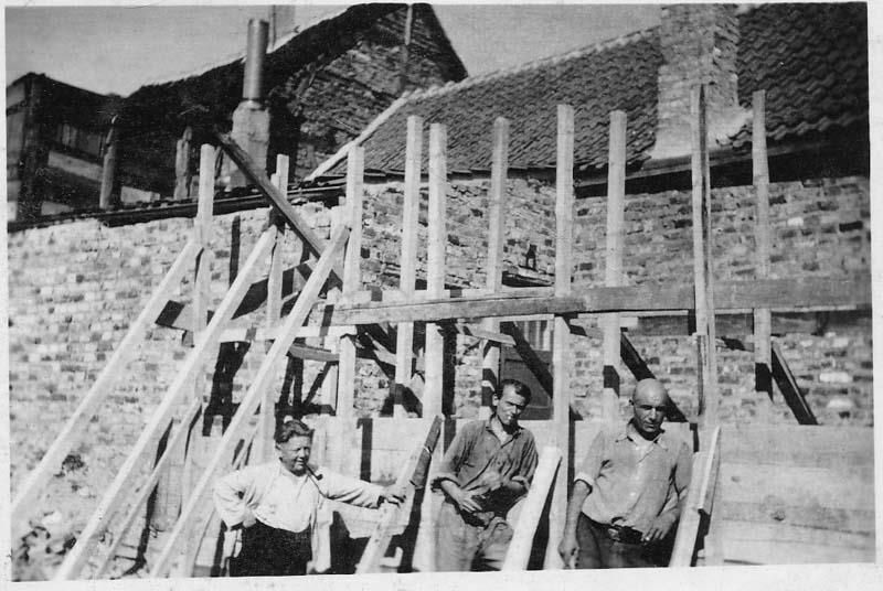 Ein Schwarzweißfoto einer Gruppe von Männern, die vor einem im Bau befindlichen Gebäude stehen