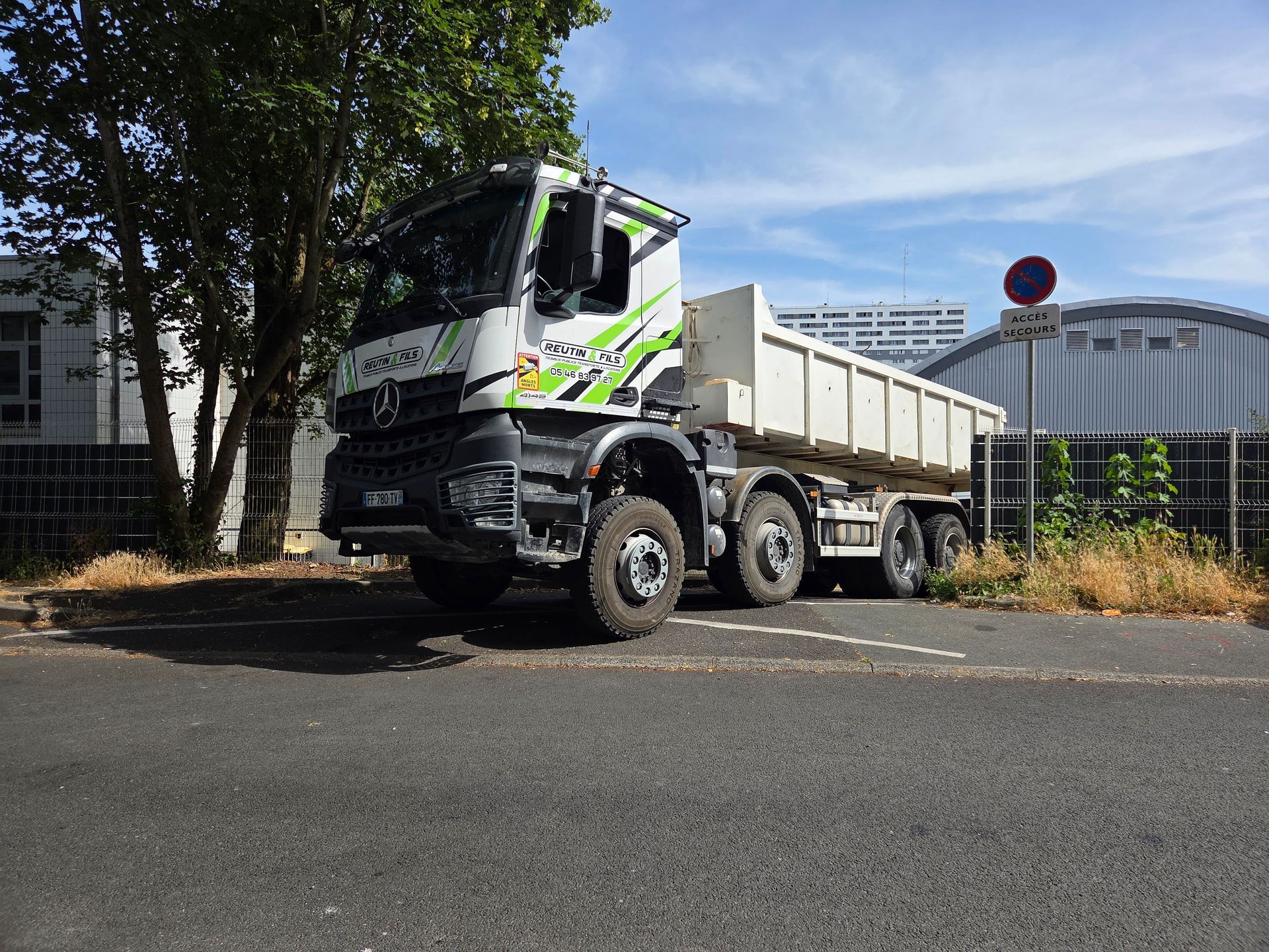 Un camion-benne blanc et vert est stationné sur l'asphalte.