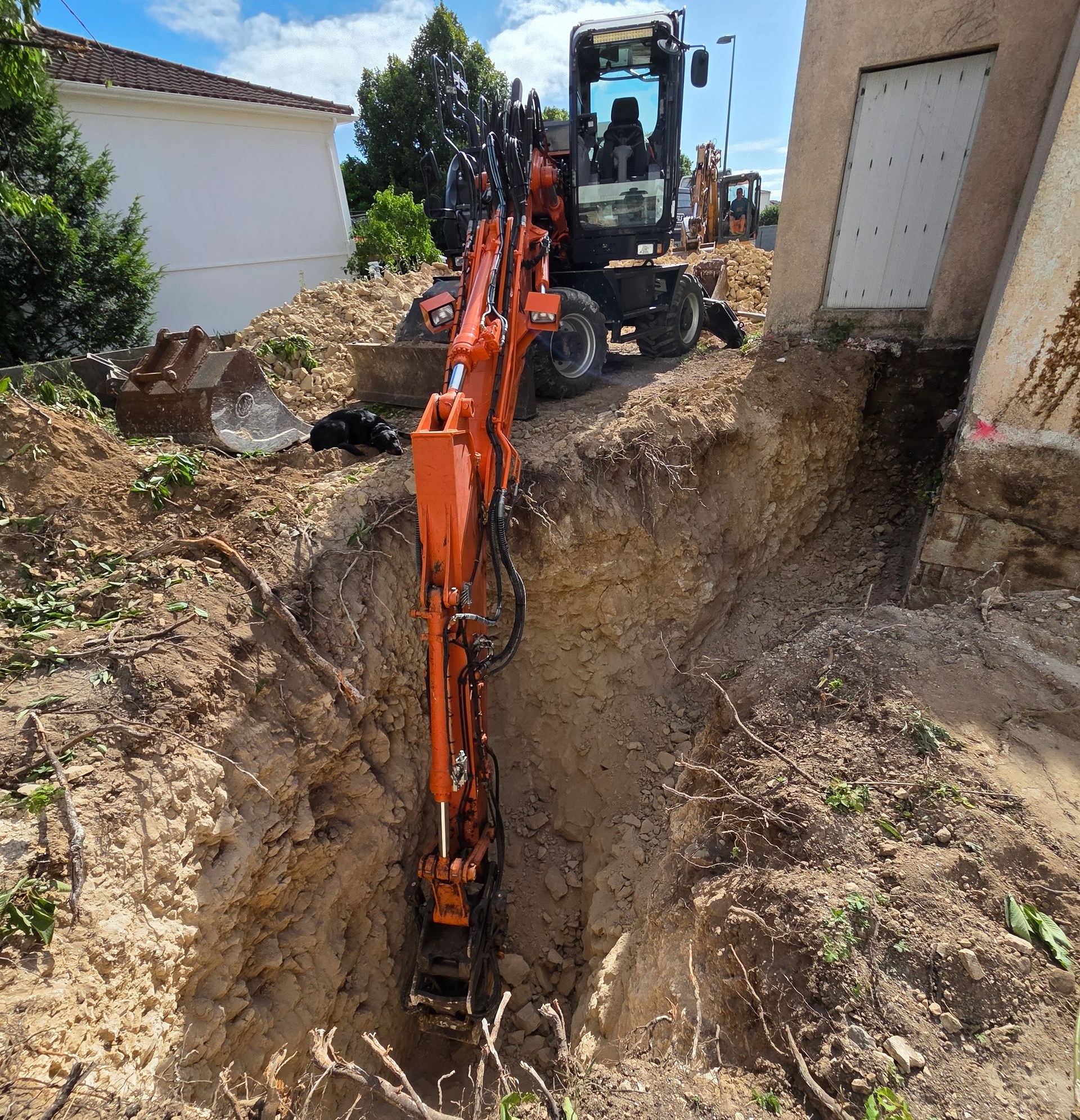 Une pelleteuse orange creuse une tranchée près d'un bâtiment.