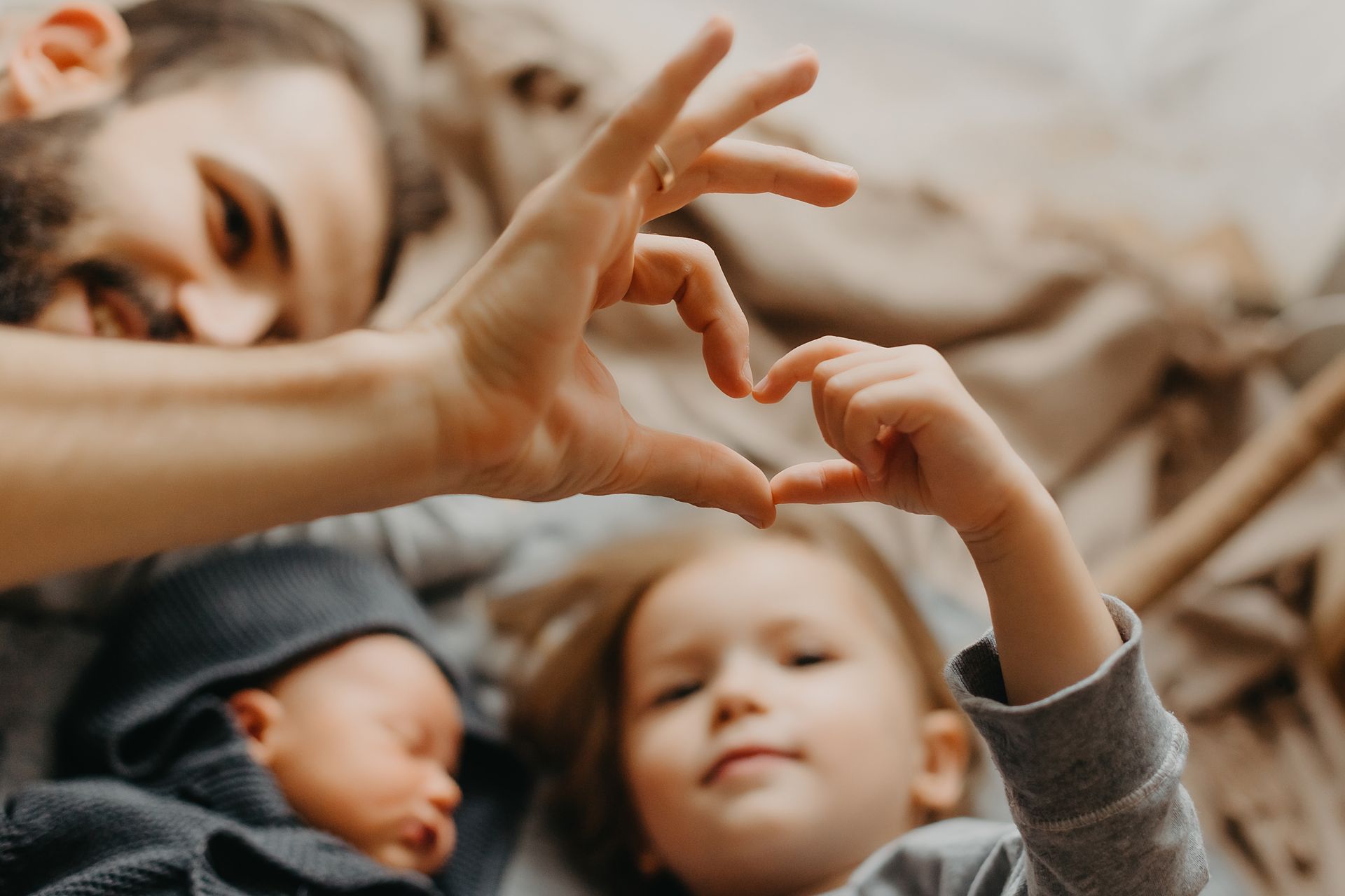 Petite fille et son père faisant un cœur avec leurs doigts, un nouveau-né entre eux