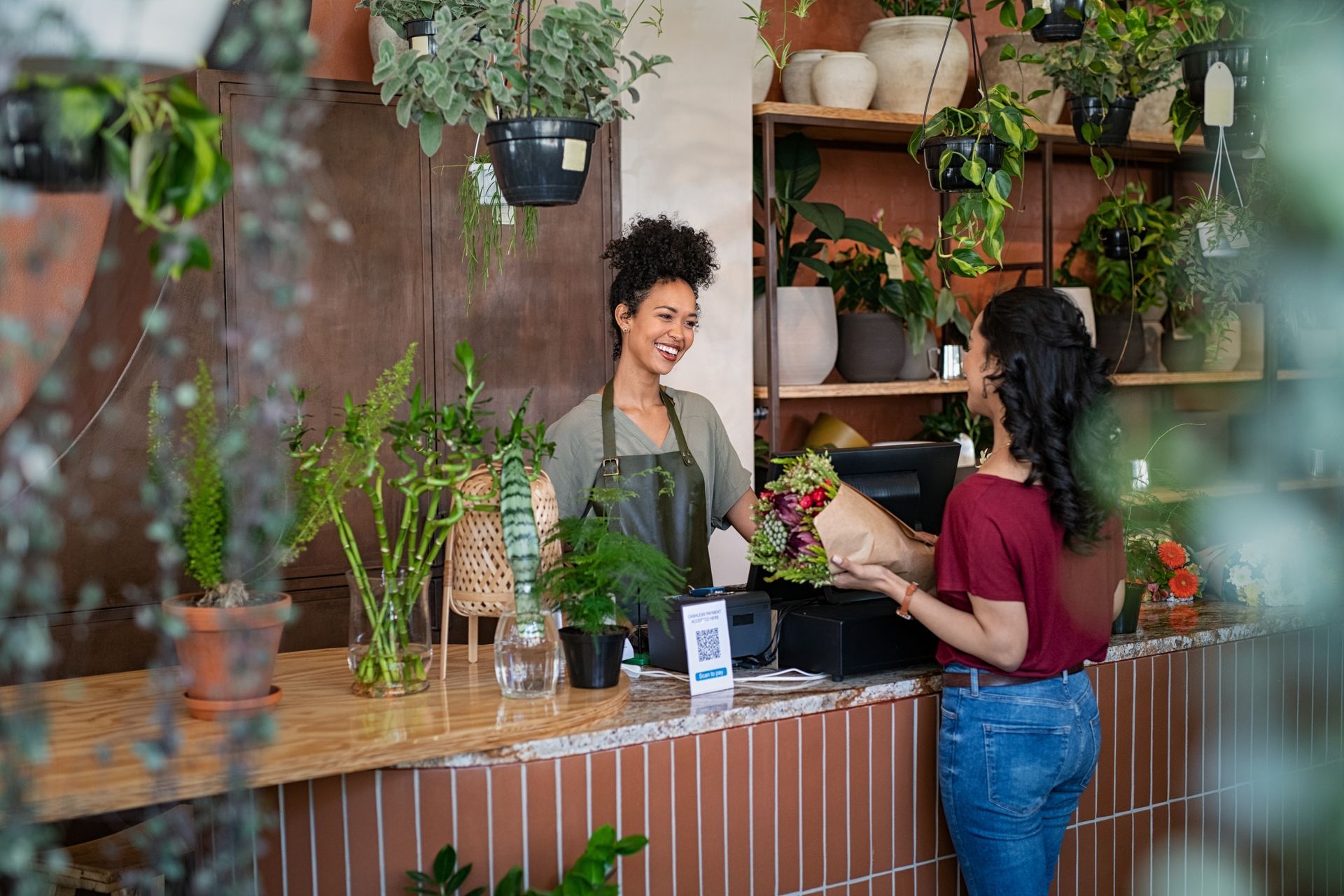 Fleuriste derrière un comptoir vendant un bouquet rouge, pourpre et vert à une cliente