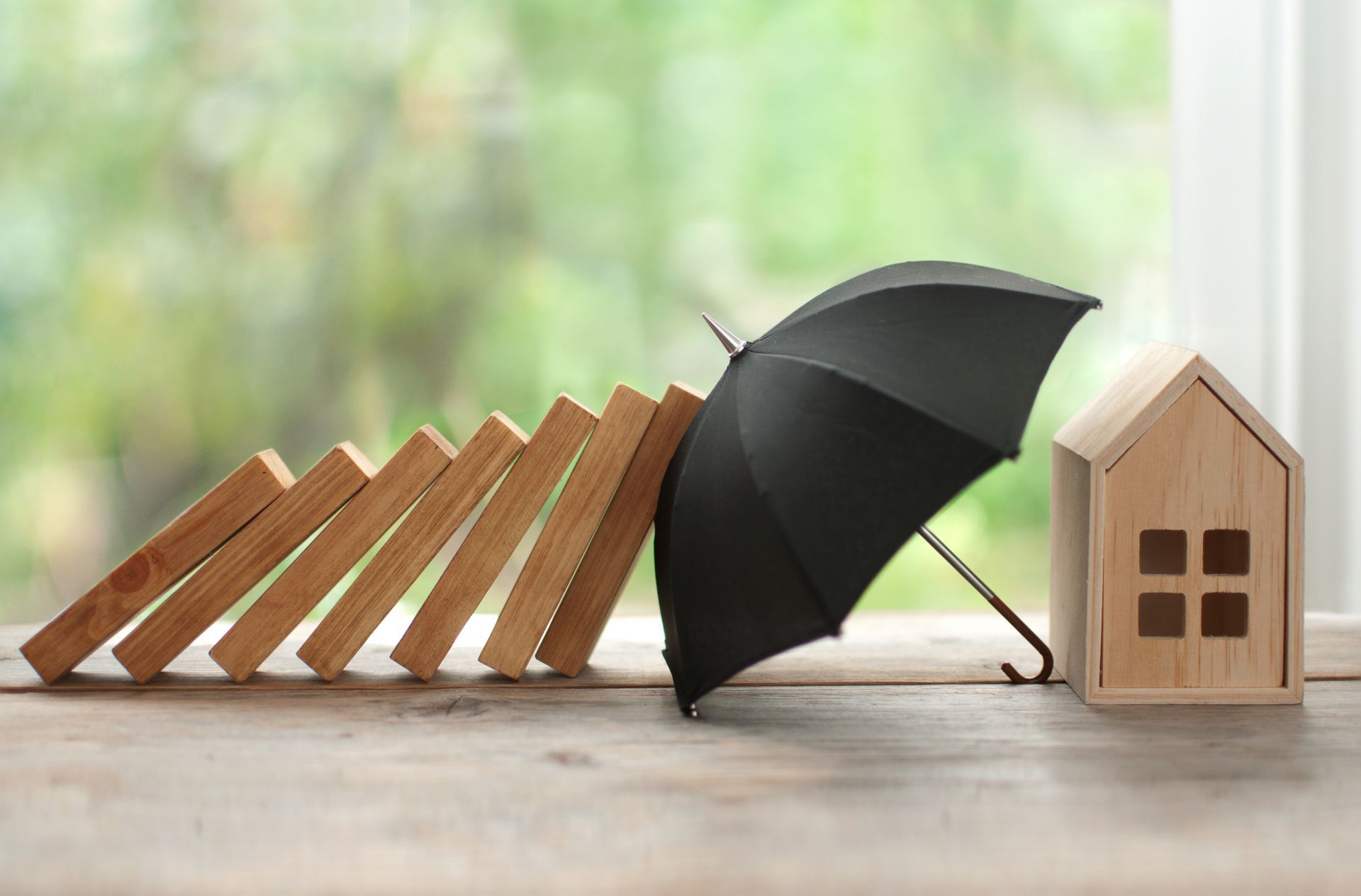 Un parapluie protège une maquette de maison d'une chute de dominos