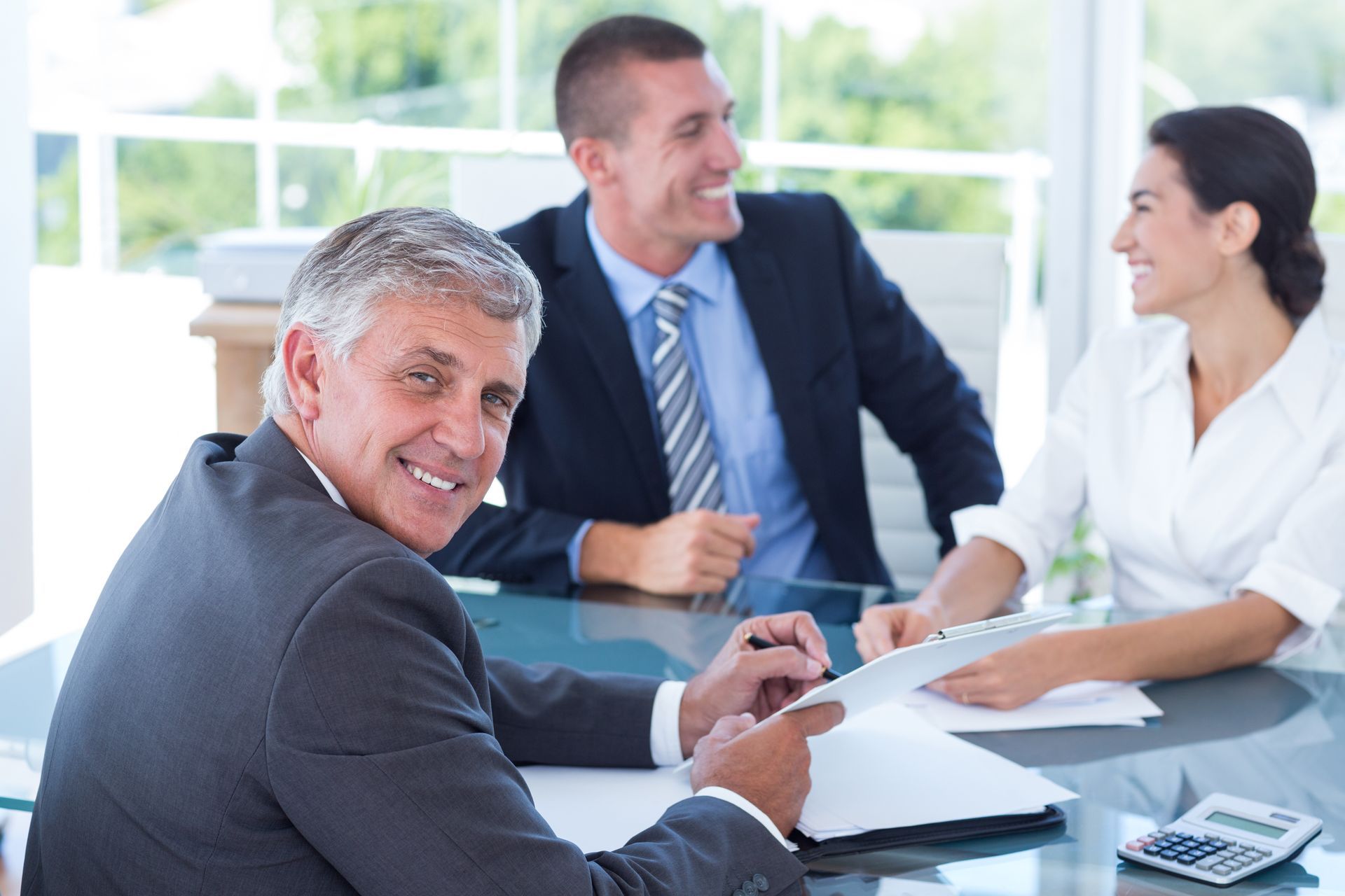 Réunion de travail dans un bureau lumineux, trois collègues souriant autour d'une table de conférence