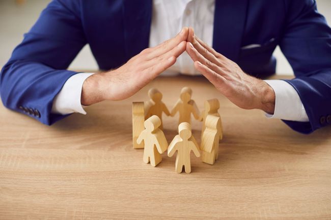Un professionnel protège de ses mains des personnages en bois représentant des salariés