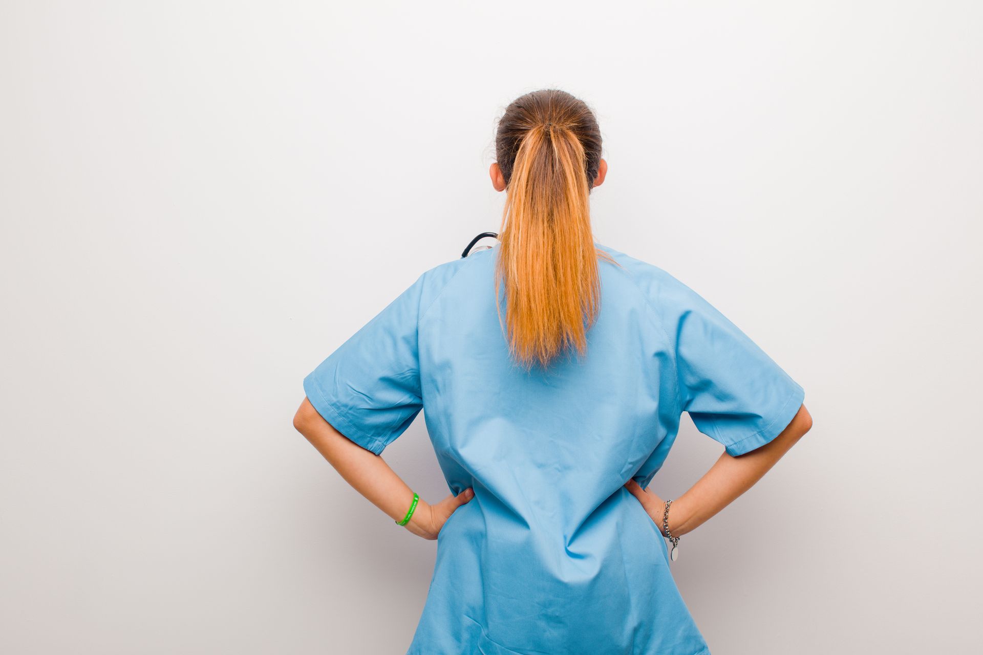 Professionnelle de la santé en blouse bleue, les mains sur les hanches, de dos.