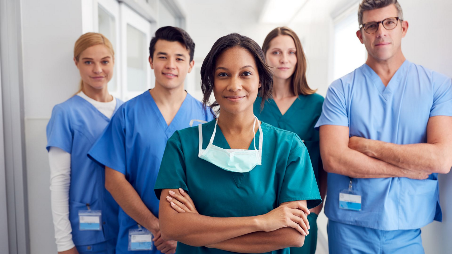 Une équipe médicale de cinq personnes en tenue médicale, les bras croisés, souriant, dans un couloir.