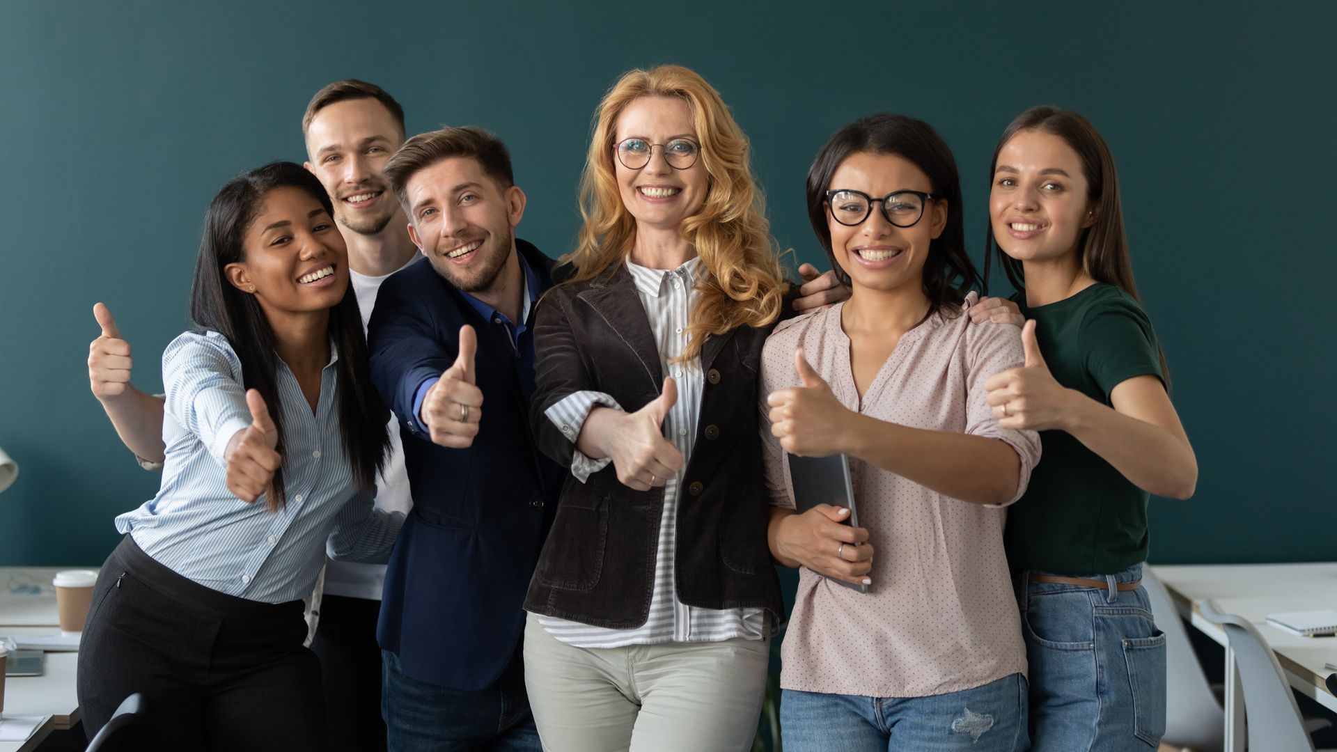 Groupe d'employés de bureau souriant et levant le pouce, devant un mur bleu.