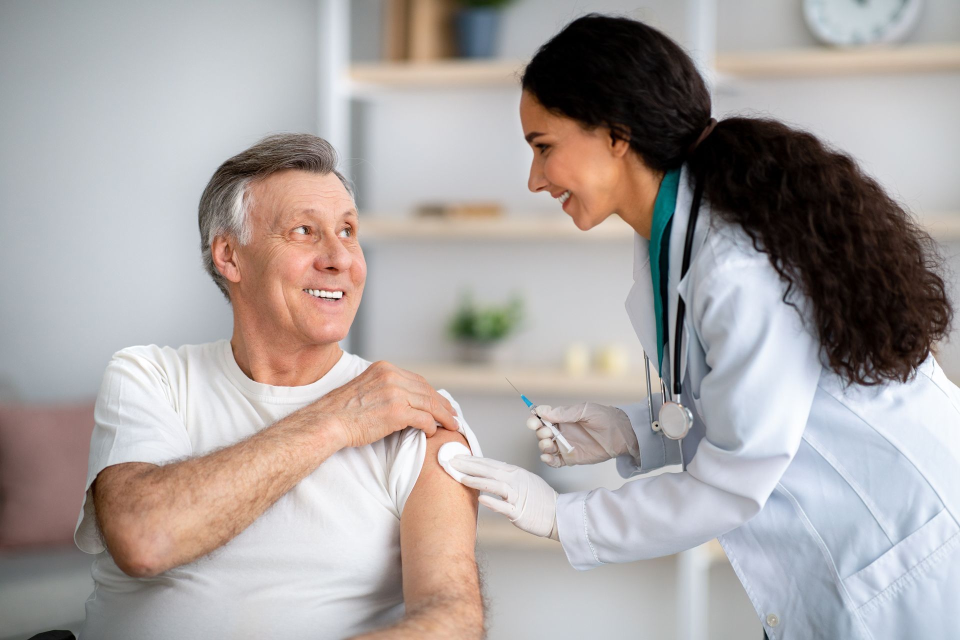 Un médecin administre un vaccin à un homme âgé à l'intérieur. Tous deux sourient.