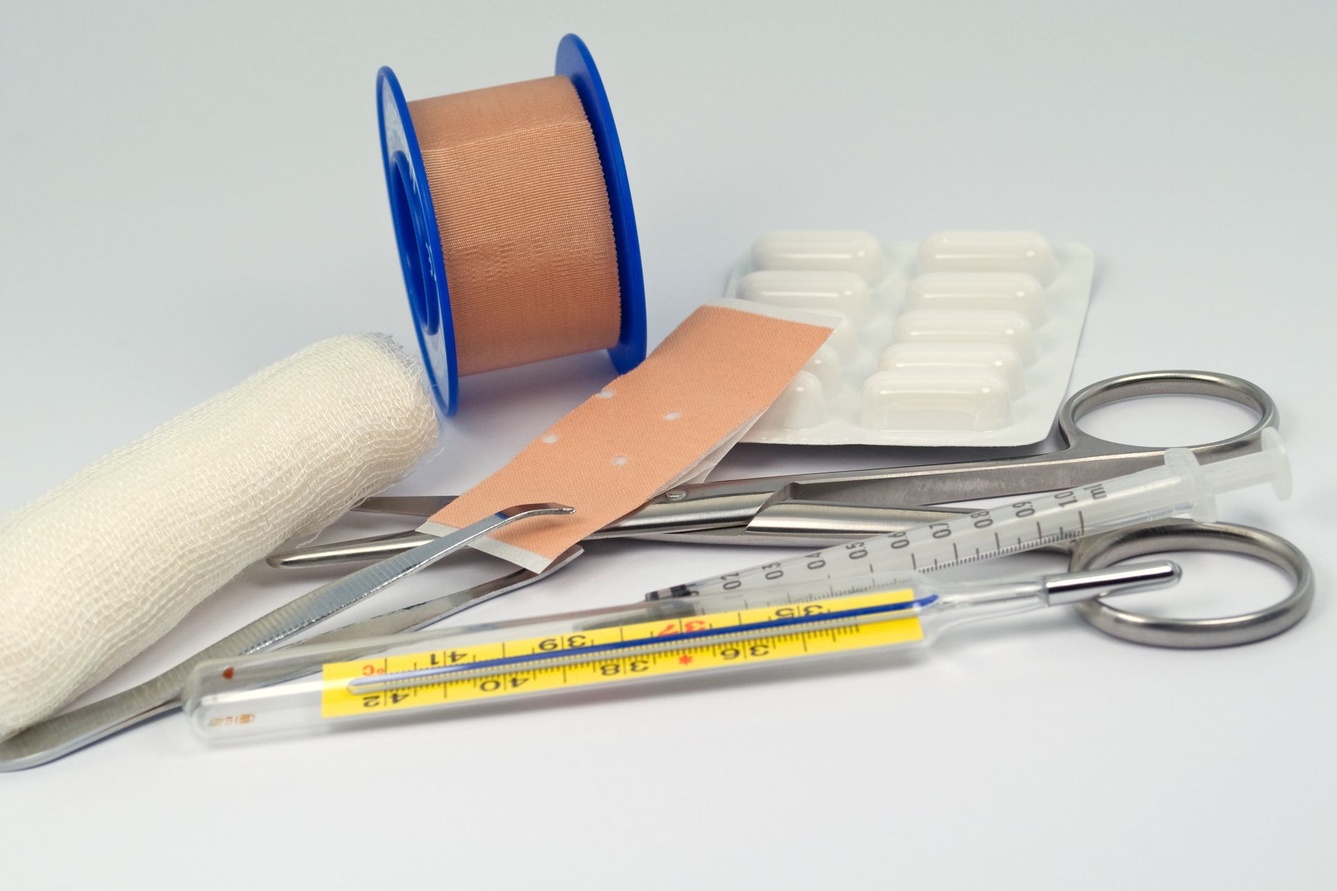 Fournitures médicales : rouleau de pansement, ruban adhésif, gaze, ciseaux, pilules, thermomètre et seringue.